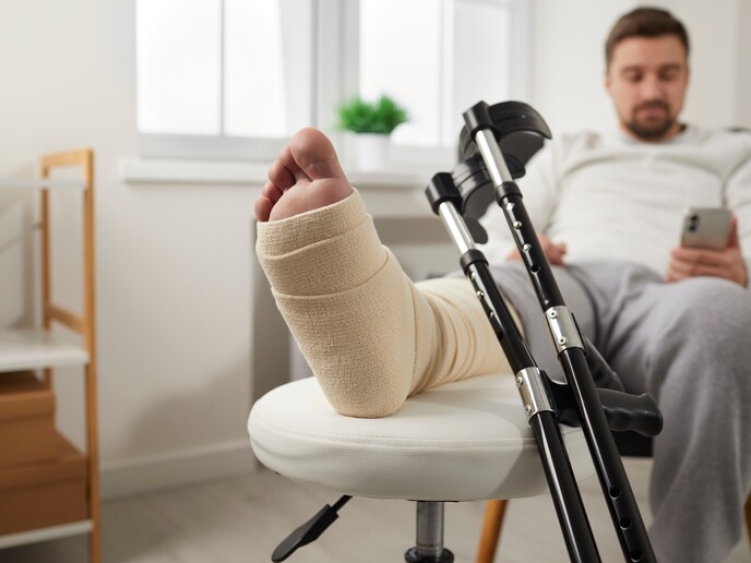 Fokus på gipset fot og krykker, mens vi ser uklart i bakgrunnen mannen som har den skadete foten